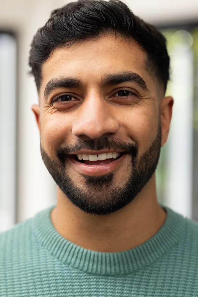 smiling young indian man in casual sweater looking utc